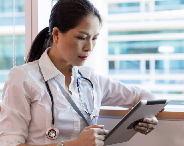 Focused female doctor using a tablet for patient records at MD Urgent Care clinic.
