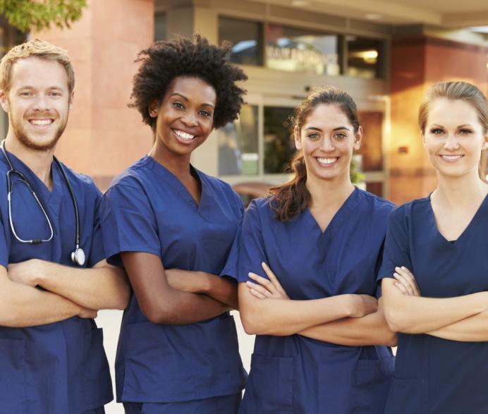 Diverse team of smiling healthcare professionals in blue scrubs standing outside a medical clinic