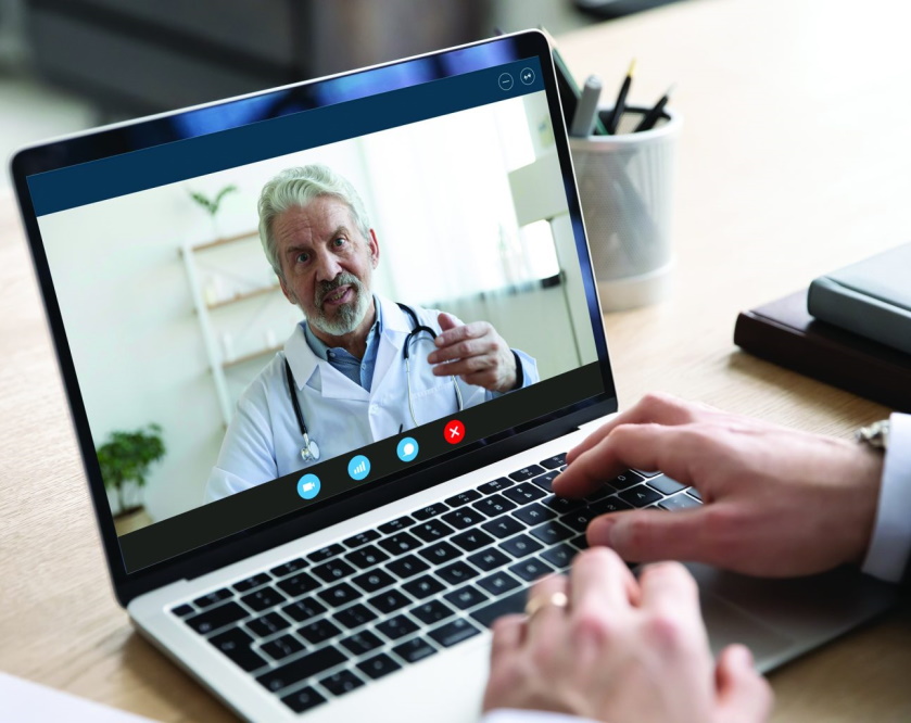 Person having an online video consultation with a senior male doctor on a laptop